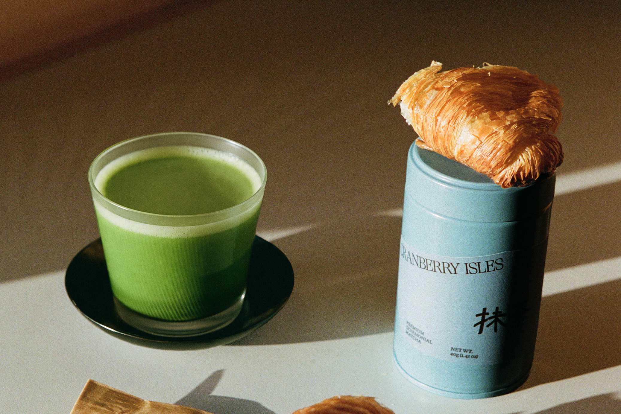 Matcha latte with Cranberry Isles matcha tin and a torn croissant 